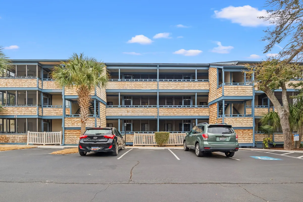 This image captures the exterior of Summertree Village with palm trees swaying near the parking lot and the building facade visible, conveying a relaxed, tropical atmosphere. Residents can be seen on the balconies, hinting at social interaction and a community vibe.