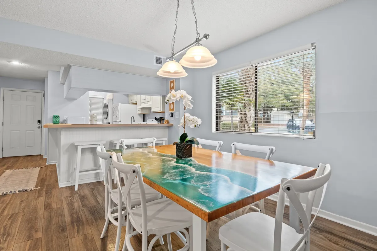A bright, cheerful dining area with a colorful table set for a meal, highlighted by an elegant orchid centerpiece and natural light streaming through a large window. The scene is inviting and suggests a space designed for family meals or friendly gatherings.