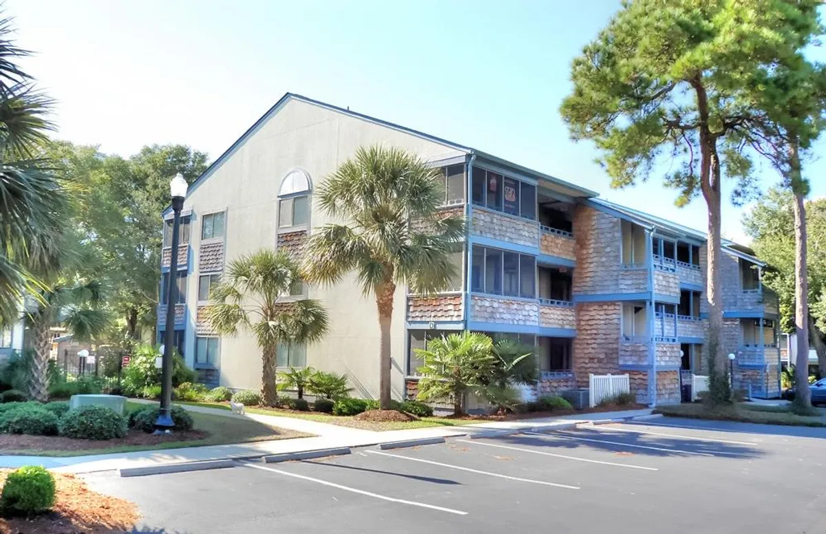 An exterior view of the condo building surrounded by palm trees, with balconies that overlook tranquil open spaces and a stone facade that hints at upscale resort living. The area is inviting for relaxing outdoors and enjoying the landscape.