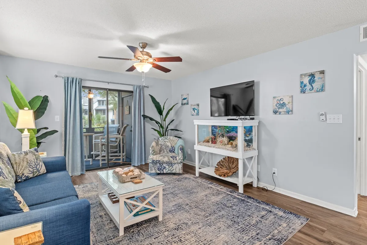 The image showcases a tastefully decorated condo living room with a cozy sofa adorned with blue cushions, a stylish light-colored coffee table, a vibrant decorative fish tank, and lush tropical plants by the window. The overall atmosphere is casual, inviting, and perfect for relaxation or gathering with friends and family.